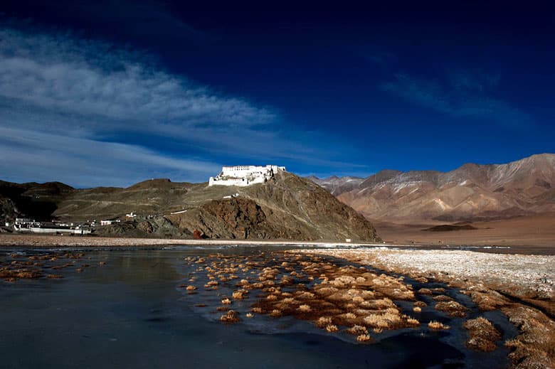 Hanle Monastery perched on a hill with mountains and water in the foreground