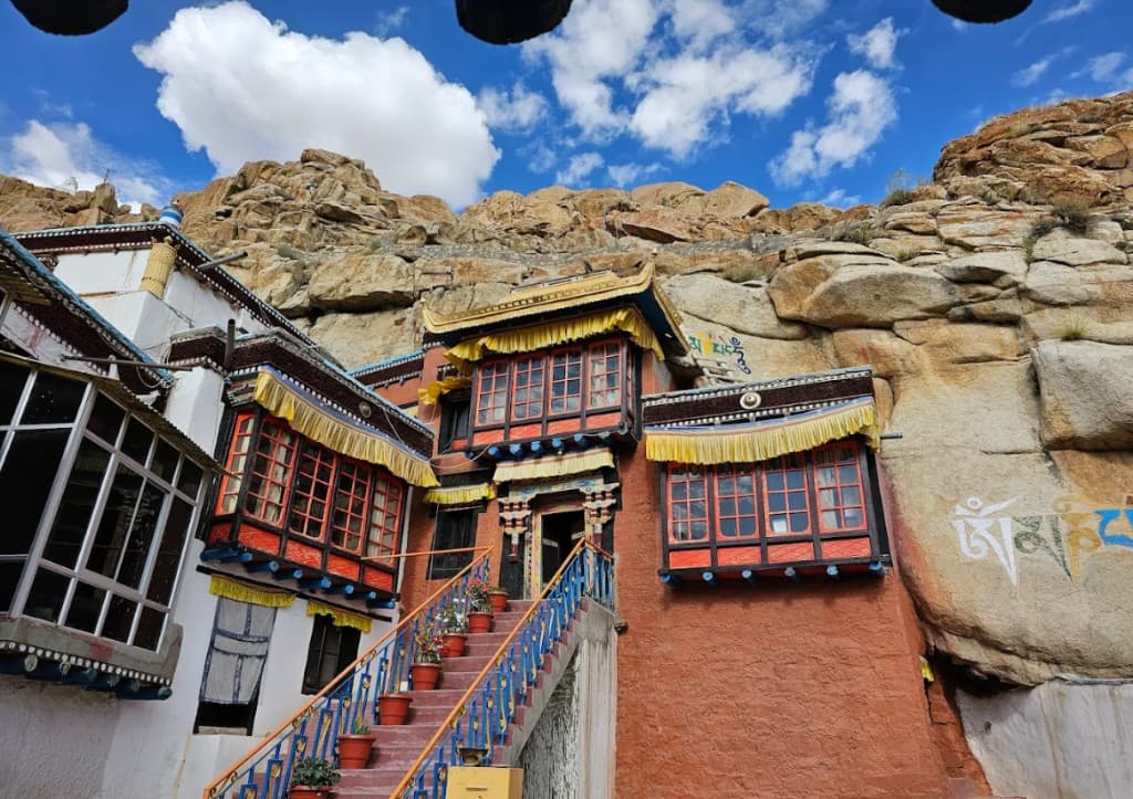 Takthok Monastery with red and white walls built into a rocky cliffside under a blue sky