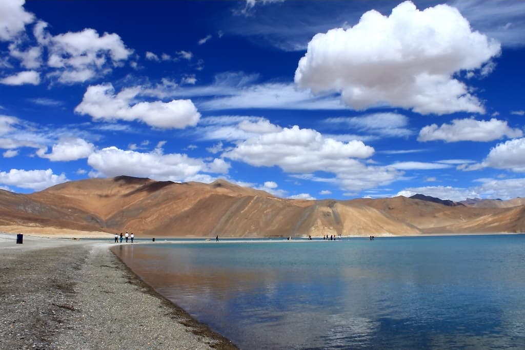 Wide panoramic view of Pangong Lake with blue water, mountains, and cloudy sky
