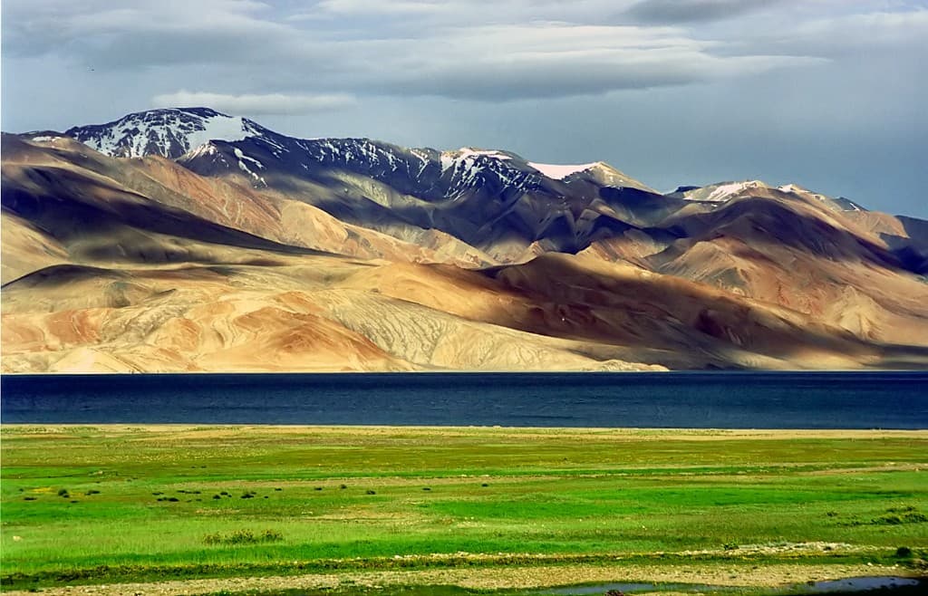 Tso Moriri lake with green meadow, blue water, and snow-capped mountains